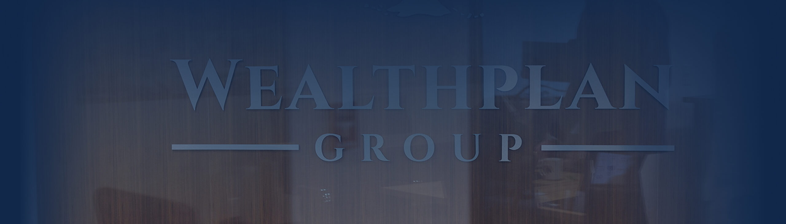 The image shows a glass door or wall with the words WEALTHPLAN GROUP etched in large, capital letters. A faint office reflection hints at a professional setting, suggesting this is a financial advisor Omaha location against a deep blue backdrop.